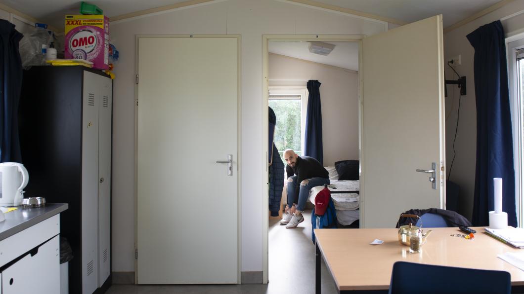 Foto van interieur stacaravan, Masaoud zit in de slaapkamer.